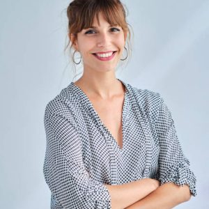 Vertical image of an adult woman smiling with her arms crossed looking at camera indoor